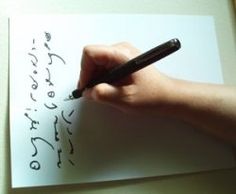 a person writing on a piece of paper with a pen in their left hand,