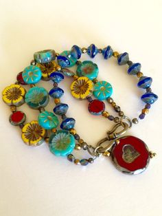 "Colorful bohemian style Czech glass multi strand flower bracelet with vintage bronze clasp and large Czech glass red heart bead charm. Bracelet is made of three separate but attached beaded strands of gorgeous Czech glass beads including: Sunflower yellow Picasso chunky pansy Cobalt blue Picasso UFO beads Turquoise/teal opaque gilded gold daisy coin beads Turquoise Hawaiian flower coral/teal/ turquoise beads Red Czech lentil beads Metallic bronze Czech fire polished faceted beads Gunmetal Czech Bohemian Single Strand Beaded Bracelets As Gift, Bohemian Jewelry With Heart Beads In Flower Shape, Bohemian Czech Glass Jewelry With Heart Beads, Bohemian Bracelets With Single Strand Round Beads, Bohemian Single Strand Bracelets With Round Beads, Bohemian Glass Jewelry With Heart Beads, Czech Beads Jewelry, Big Bracelets, Czech Glass Jewelry