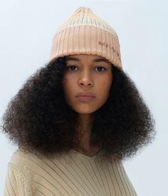 a woman with curly hair wearing a knitted hat and looking off to the side