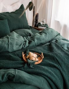 a basket with a stuffed animal in it sitting on a green comforter covered bed