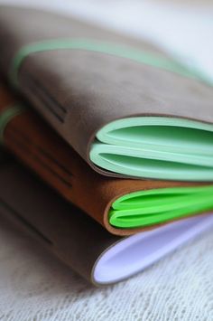 three leather folders stacked on top of each other with green and white papers sticking out of them