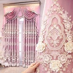 the curtains are pink with white flowers on them and they are being held up by someone's hand