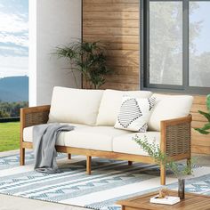 a white couch sitting on top of a wooden floor next to a window and potted plant