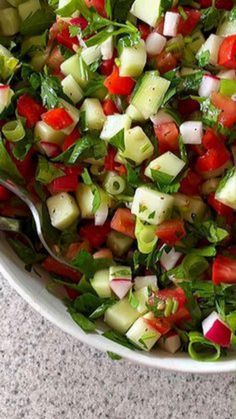 a salad with cucumbers, tomatoes and lettuce in a white bowl