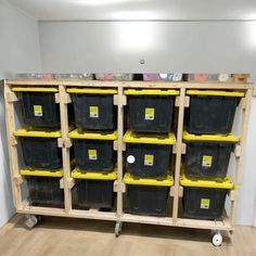 several black and yellow bins are stacked up on a wooden cart in a room