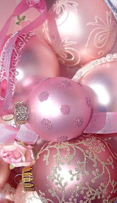 some pink and gold ornaments are in a bowl with ribbons on it's sides