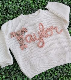 a white sweater with the word taylor written in pink on it and flowers embroidered across the chest