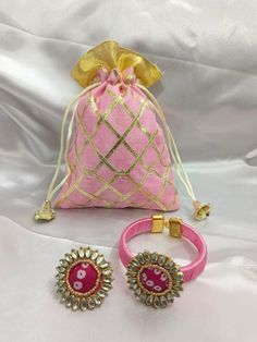 two pieces of jewelry sitting on top of a white cloth covered bed next to a bag