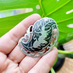 a hand holding a silver and black brooch with an image of a dragon on it