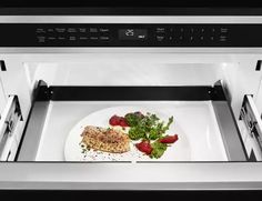 a white plate with meat and vegetables in an open microwave door on a counter top