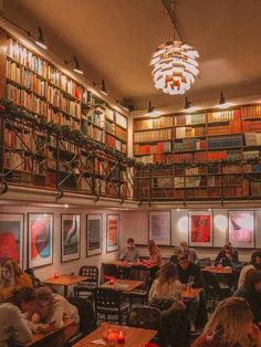 people sitting at tables in a library with bookshelves and paintings on the walls