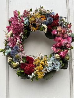 a wreath made out of flowers on the side of a white door with green leaves