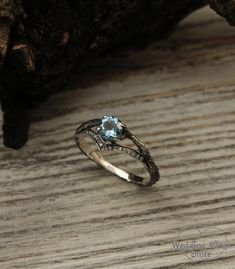 a silver ring with a blue topazte stone sits on a piece of wood