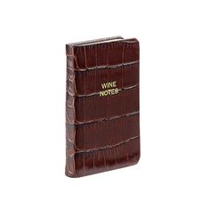 a brown alligator skin notebook with wine notes written on the front and back cover, in gold lettering