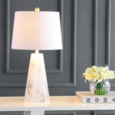 a white table lamp sitting on top of a desk next to a vase with flowers