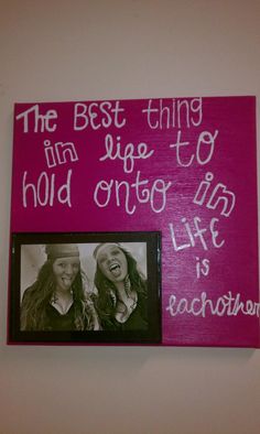 two women are smiling and laughing in front of a pink sign that says the best thing i'm huge to hold onto life is each other