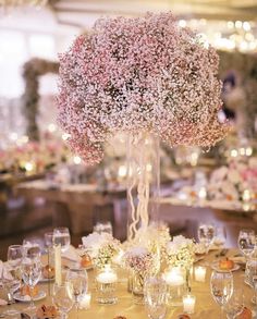 a centerpiece with flowers and candles on a table in a room filled with tables