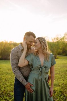 a man and woman standing next to each other in front of a field at sunset