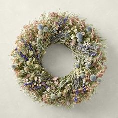 a dried wreath with lavenders and bluebells is hanging on the white wall