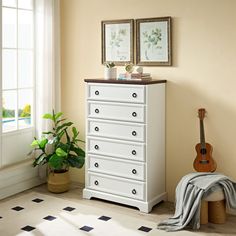 a white dresser sitting in front of a window next to a potted green plant