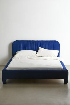 a bed that is made up with white sheets and blue headboard on top of it