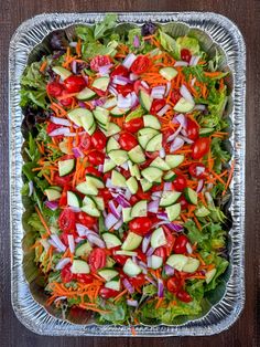 a salad with cucumbers, tomatoes, carrots and lettuce in a tin pan