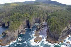 an aerial view of the ocean and rocky coastlines near some forested hills with trees on them