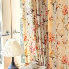 a table with a cup and saucer on it next to a window covered in curtains