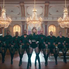 a group of women in black outfits standing next to each other with chandeliers hanging from the ceiling