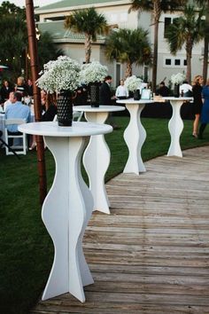 two white tables with vases and flowers on them at an outdoor event in front of palm trees