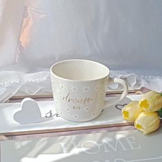 a white coffee cup sitting on top of a table next to some yellow tulips