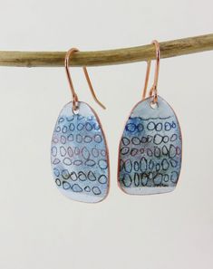 two small blue and white earrings hanging from a tree branch with copper earwires