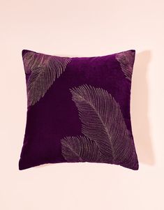 a purple and gold feathered pillow on a pink background