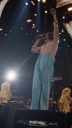 a woman standing on top of a stage holding her hands up in the air while singing