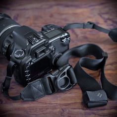 a black camera sitting on top of a wooden table next to a strap that is attached to it