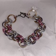 9 1/4" Large Chain Mail Bracelet. This Features Anodized Aluminum Links In The Colors Of Silver, Gunmetal, Brass, And Pink. There Is A Pewter Toggle Used As A Closure. I Can Make This Longer Or Shorter Upon Request.