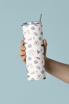 a hand holding a white tumbler cup with various items on it and a blue background