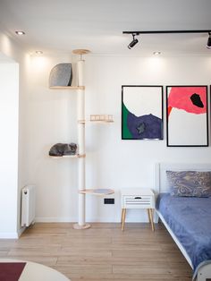 a bedroom with white walls and wooden flooring, two paintings on the wall next to a bed