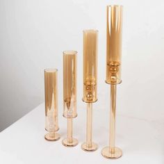 three tall glass vases sitting next to each other on a white counter top in front of a white wall