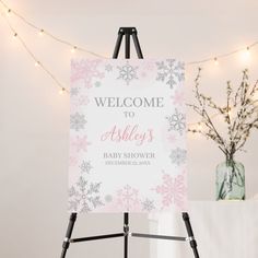 a welcome sign for a baby shower is displayed on an easel with lights in the background