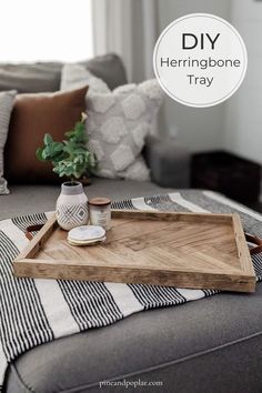 a wooden tray sitting on top of a couch next to a vase and potted plant