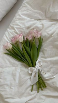 a bouquet of pink tulips tied with a white ribbon on top of a bed