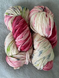 several skeins of yarn sitting on top of a gray blanket covered in white and pink colors