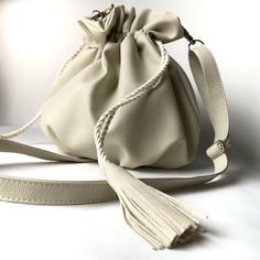 Bag made of extremely high quality synthetic material in off white. The lining is made with beige velvet, has an inner pocket with a zipper closure. All hardware is silver and the handle is 1.30 cm long, which can be adjusted to the desired size with the adjuster. Soft and lightweight bag with closure on the sides with drawstring and tassel at the ends made in the same material as the bag. The strap has carabiners which allow you to remove the strap. On the top it has a frilled detail that is given when closing and on the base pleats. It's great to take on trips as it can be put in your suitcase and doesn't get deformed (just open it and remove the strap to put it inside, it's important not to bend the rigid bottom).     Approximate measurements (Handmade product, slight variations may occ Large Capacity Cream Bucket Shoulder Bag, Cream Bucket Bag With Detachable Strap For Daily Use, Cream Bucket Bag With Detachable Strap, Beige Bucket Bag For Everyday Use, Everyday Use Beige Bucket Bag, Beige Bucket Bag With Detachable Strap And Double Handle, Beige Bucket Bag With Removable Pouch As Shoulder Bag, Neutral Bucket Bag With Adjustable Strap For Daily Use, Cream Bucket Shoulder Bag With Removable Pouch