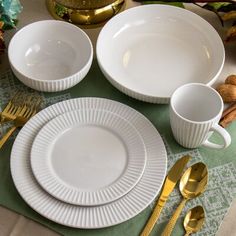 the table is set with white dishes and gold utensils