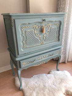 an old dresser painted in blue and gold with a white rug on the floor next to it