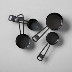 four black pans with handles and spoons on a white surface, top view