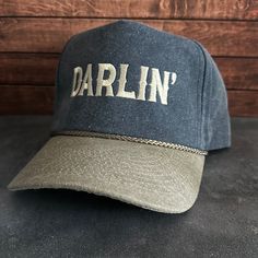 Vintage Style Darlin' Embroidered Faded Canvas Snapback Trucker Rope Hat with Free Shipping. White stitched text/logo. Condition is "New with tags". Shipped with USPS First Class. Step into the world of the great outdoors with our Darlin' Stitched Faded Canvas Rope Hat. With its faded canvas and rope accents, this hat exudes rustic charm and pays tribute to the iconic country music legends. Plus, enjoy free shipping on this vintage-inspired accessory that's perfect for any country music enthusia Vintage Cotton Snapback Hat With Embroidered Logo, Vintage Adjustable Trucker Hat With Letter Print, Vintage Cotton Hat With Letter Print, Faded Vintage Cap, Vintage Snapback Hat With Letter Print For Outdoor, Vintage Letter Print Snapback Hat For Outdoor, Vintage Faded Cap, Faded Vintage Hat, Vintage Faded Cotton Baseball Cap