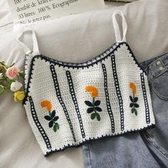 a white crocheted top with orange flowers on it next to jeans and a book