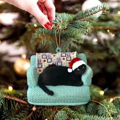 a black cat ornament hanging from a christmas tree with a santa hat on it